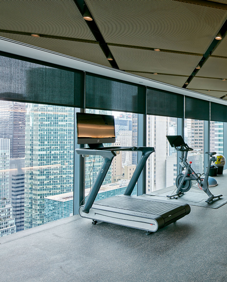 Interior view of the private wellness gym with a contemporary interior design, equipped with a treadmill and a bike on a rubber motion isolated raised floor, promoting an active lifestyle for the employees. Those who use this equipment have a multi-million dollar view looking at the skyscrapers of Midtown Manhattan.