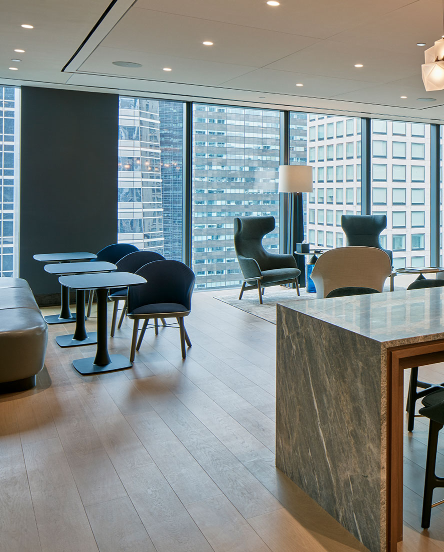 An expansive modern office collaboration area with a large island, mixed seating options, and bistro seating with stellar views of the skyscrapers in Midtown Manhattan's financial hub.