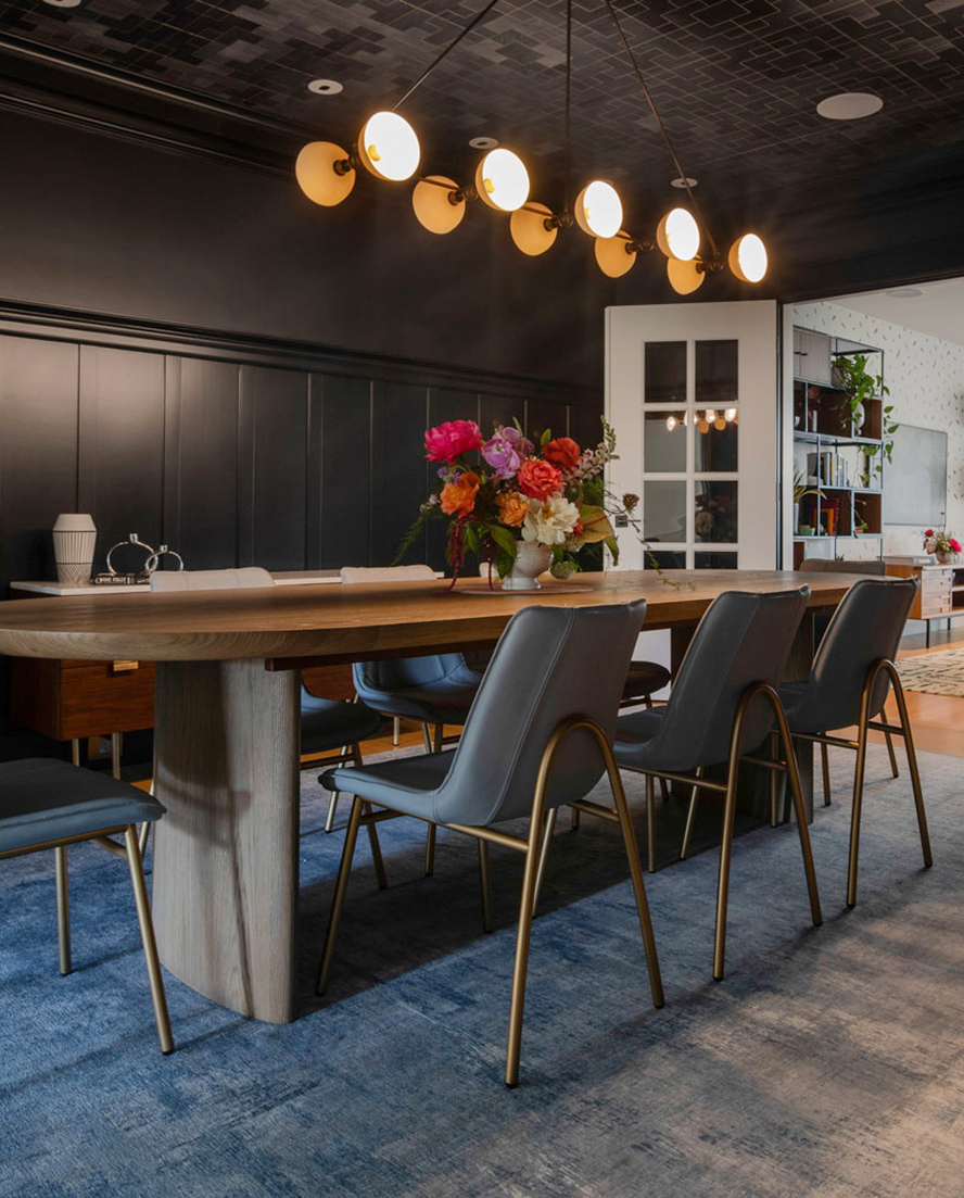 A modern dining room with a long wooden table, gray chairs, a floral centerpiece, and a contemporary linear chandelier showcases the chic elegance of Residential Interior Design by California interior design firm Urban Chalet.