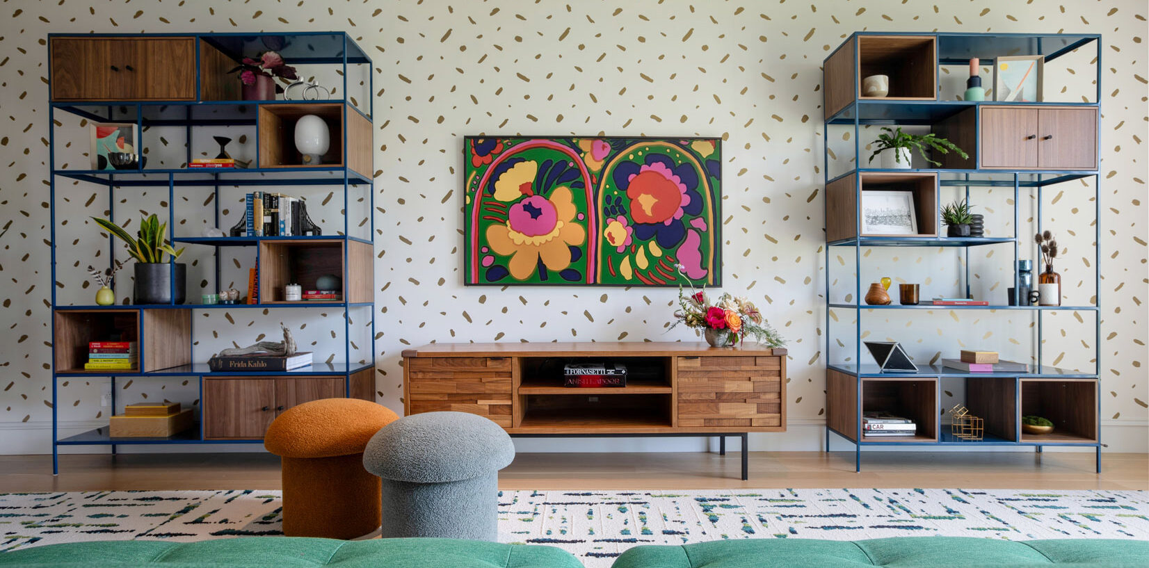 A vibrant living room featuring cheerful wallpaper and colorful modern furniture, creating a lively and inviting atmosphere for relaxation and gatherings. These cobalt blue metal bookshelves with walnut detailing are both stunning and functional, perfectly balancing family-friendly interior design.