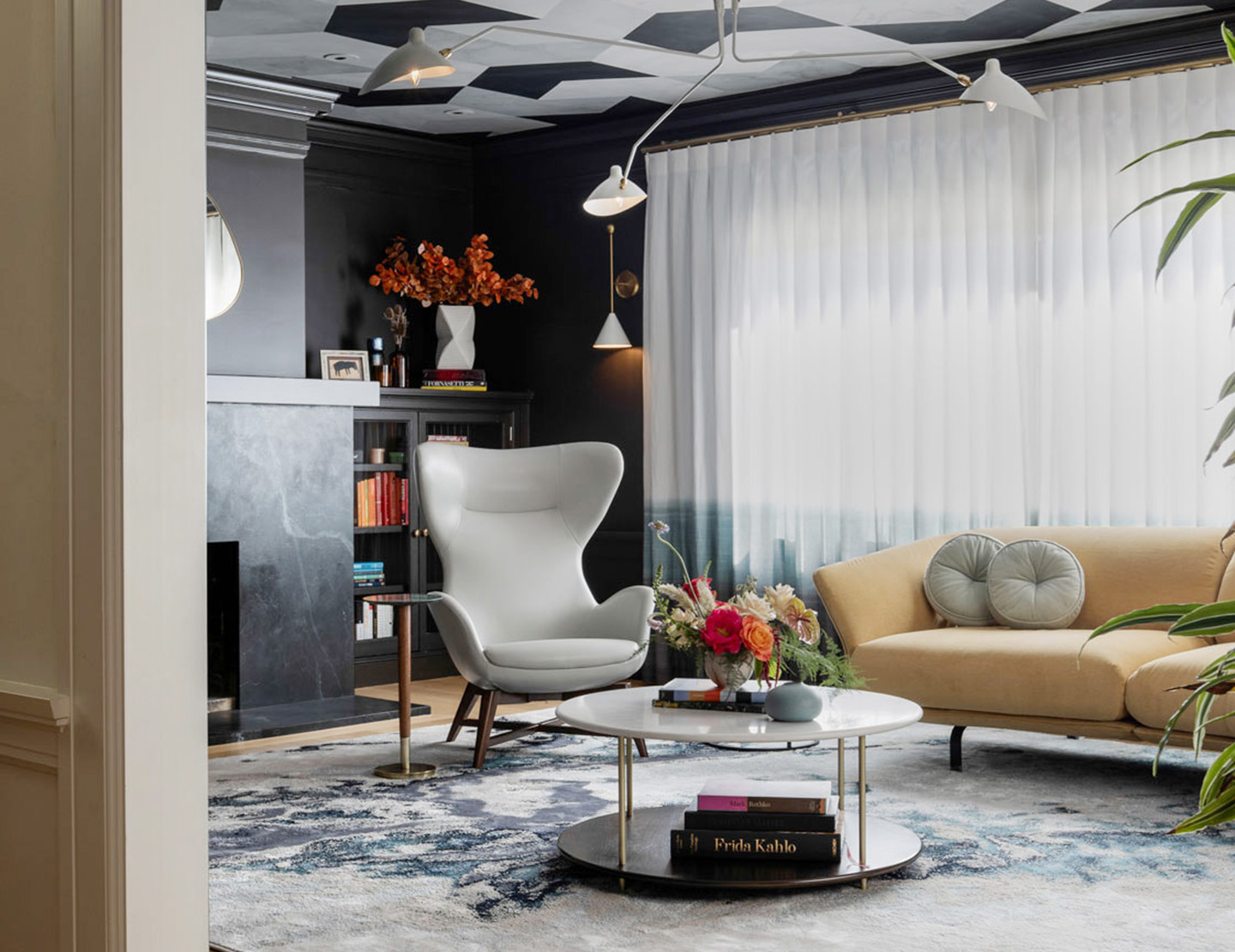 A contemporary living room showcasing black walls and a graphic ceiling paired with sleek white furniture, exuding a stylish and bold vibe. Sheer white curtains over the wide windows let the light shine through to keep the space bright and inviting.