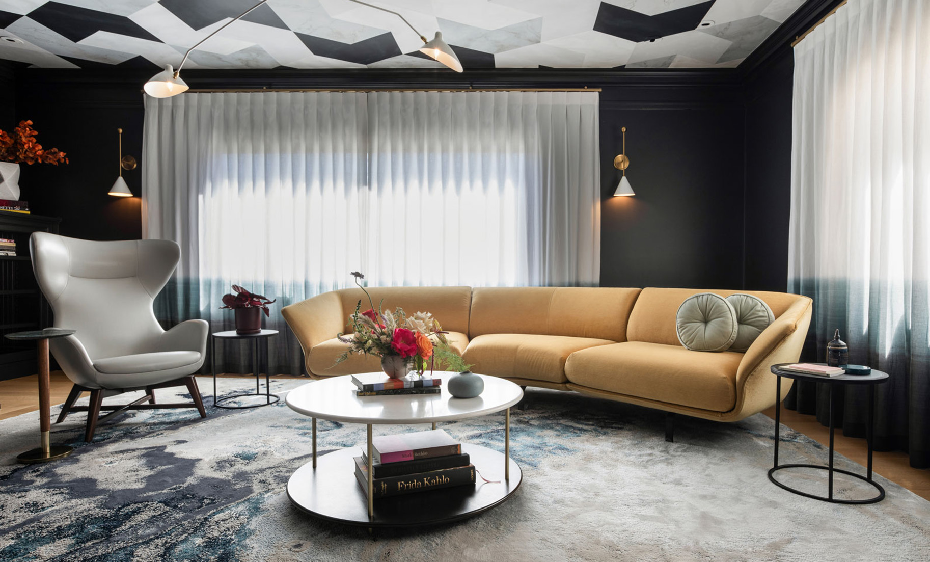 Image of a bold California living room with contemporary interior design. Features a high contrast black and white color scheme, a patterned ceiling covering, sheer white curtains, and a curved midcentury modern yellow velvet sofa. The ceiling has a white metal Mouille-style MCM light fixture.